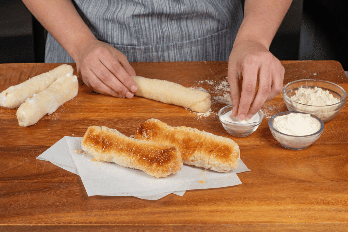 Baker hand-rolling quesito dough on a wooden table